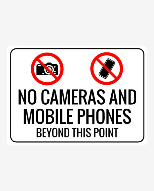A sign with a white background featuring text and symbols. The text reads 'NO CAMERAS AND MOBILE PHONES BEYOND THIS POINT.